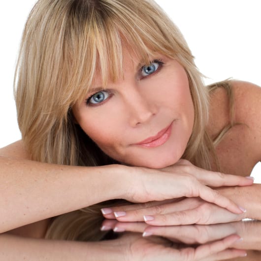 Middle-aged woman with bangs resting her chin on her folded hands.